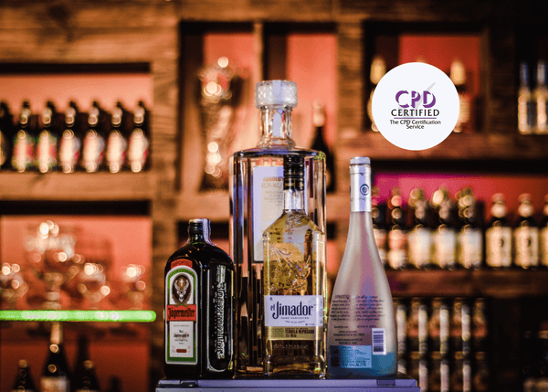 Four types of alcoholic drinks are displayed in focus on a pub counter, with a blurred background of spirits lining the full bar.