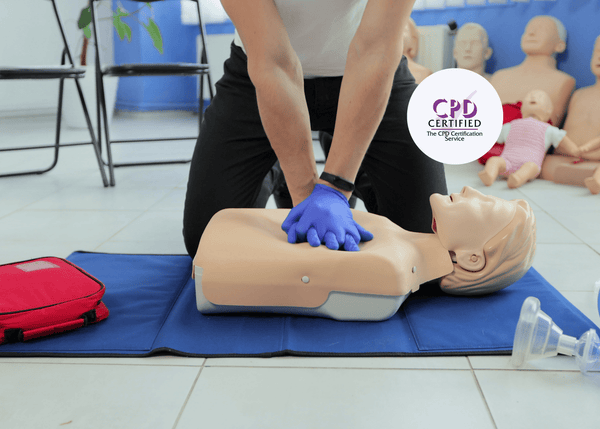 A workplace first aid instructor demonstrates CPR on a blue training mat.