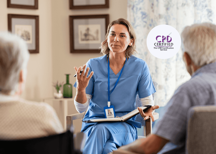 A female nurse in blue scrubs sits with an open notebook, talking to two older adults in a home environment, reflecting supportive end-of-life care discussions.