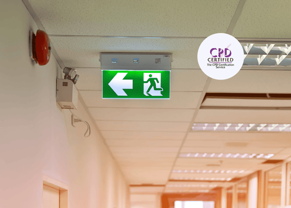 A green fire exit sign mounted on a care home ceiling beside a fire alarm, ensuring clear visibility and guidance during emergency evacuations.