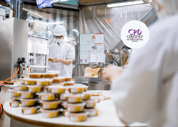 Food factory staff wearing protective clothing handle packaged meals on a production line, demonstrating hygiene and safety practices in food manufacturing.