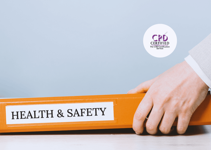 A close-up of a hand holding an orange binder labelled “HEALTH & SAFETY” placed on a light wooden desk, symbolising occupational health management.