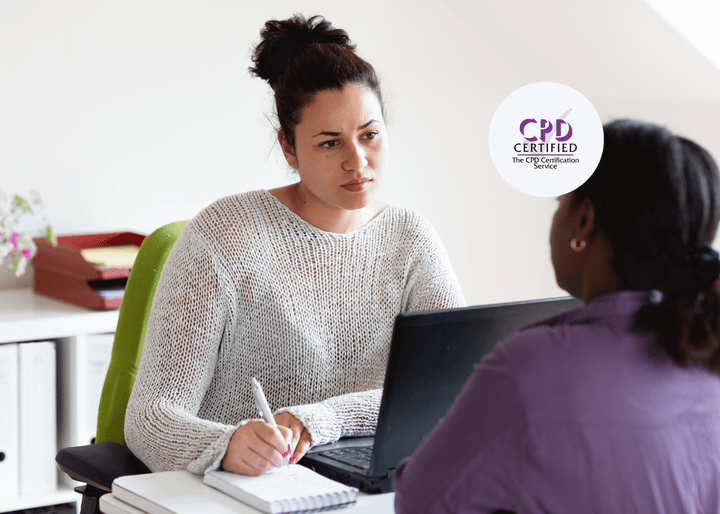 A woman in a white jumper listens attentively while taking notes during a conversation across a desk, representing support and awareness in mental health care.