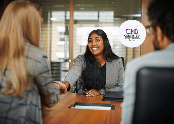 Smiling woman in a blazer reaches across a meeting table to shake hands with two interviewers during a job interview.