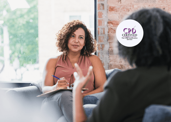 Woman with curly hair holding a pen and clipboard, attentively listening to someone during a seated discussion.