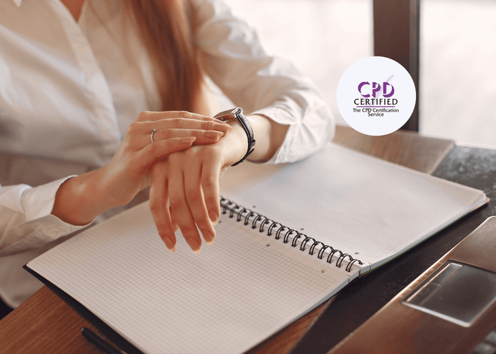 Individual in a white shirt looking at their wristwatch while sitting at a desk with an open grid notebook and pen in front of them.