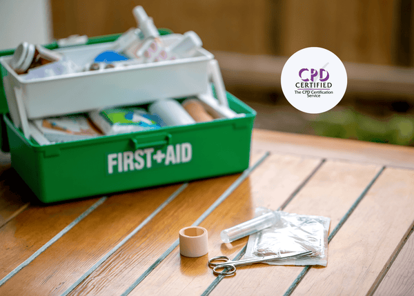 Green first aid kit on a bench with health and safety items, including scissors and tape visible outside the box.