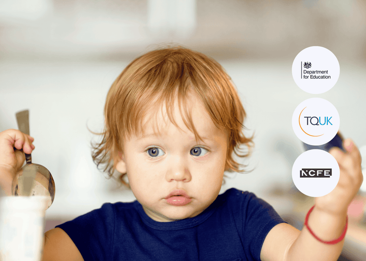 A young child with light brown hair holds a spoon and cup while looking ahead in a childcare environment, highlighting a mealtime moment.