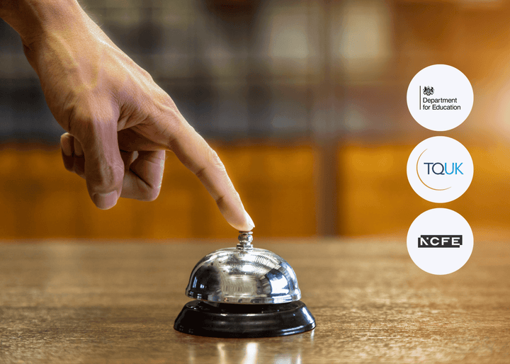 Veined hand pressing a polished silver service bell on a wooden counter in a warmly lit hospitality environment.