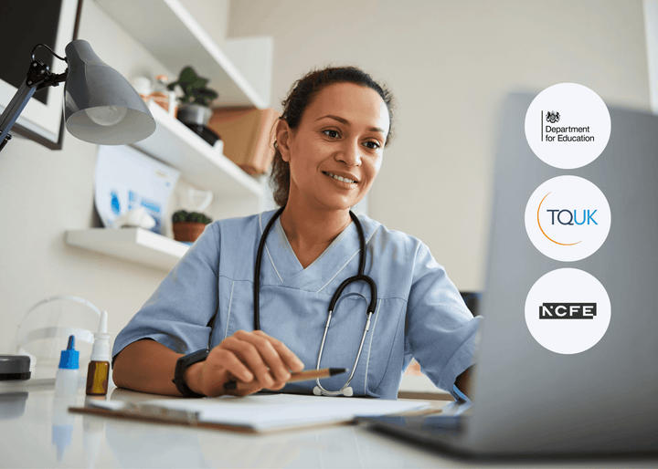 A smiling healthcare worker in scrubs with a stethoscope sits at a desk, using a laptop next to a notepad and medicine bottles, representing digital skills in care.