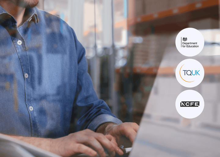 A man in a denim shirt types on a laptop inside a warehouse, with shelves and boxes blurred in the background, representing digital skills in logistics.