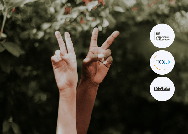 Two hands of different skin tones raised in peace signs, set against green foliage and soft natural light, symbolising unity and diversity.