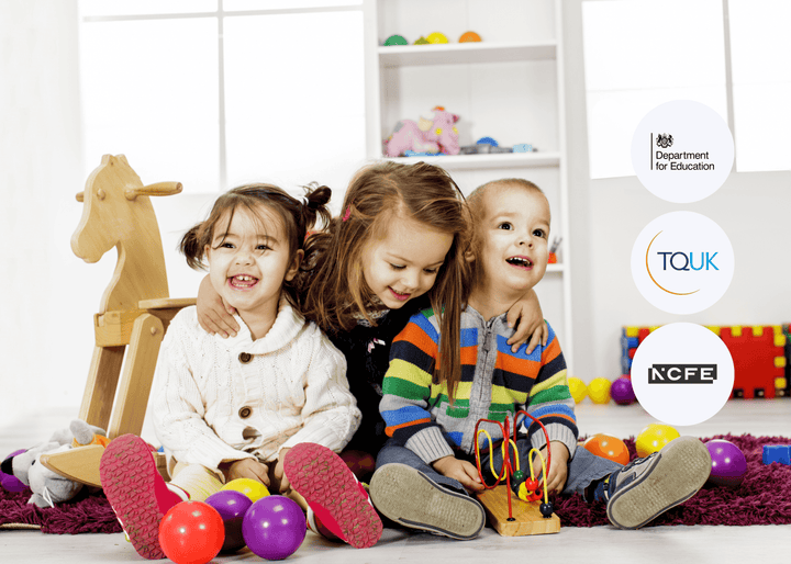 Three young children sitting on the floor playing with colourful toys, surrounded by balls and a wooden rocking horse, representing early years development.