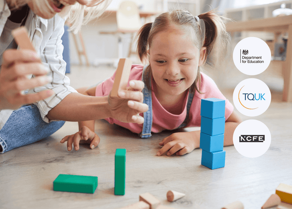 A young girl with pigtails smiles while stacking colourful wooden blocks on the floor, supported by an adult beside her, symbolising learning and development.