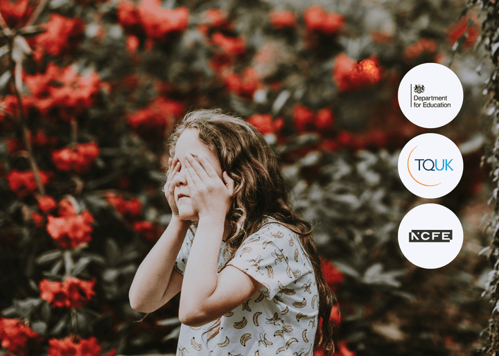 Child with long hair covering their face with both hands, standing in front of red flowering bushes, symbolising the hidden impact of adverse childhood experiences.